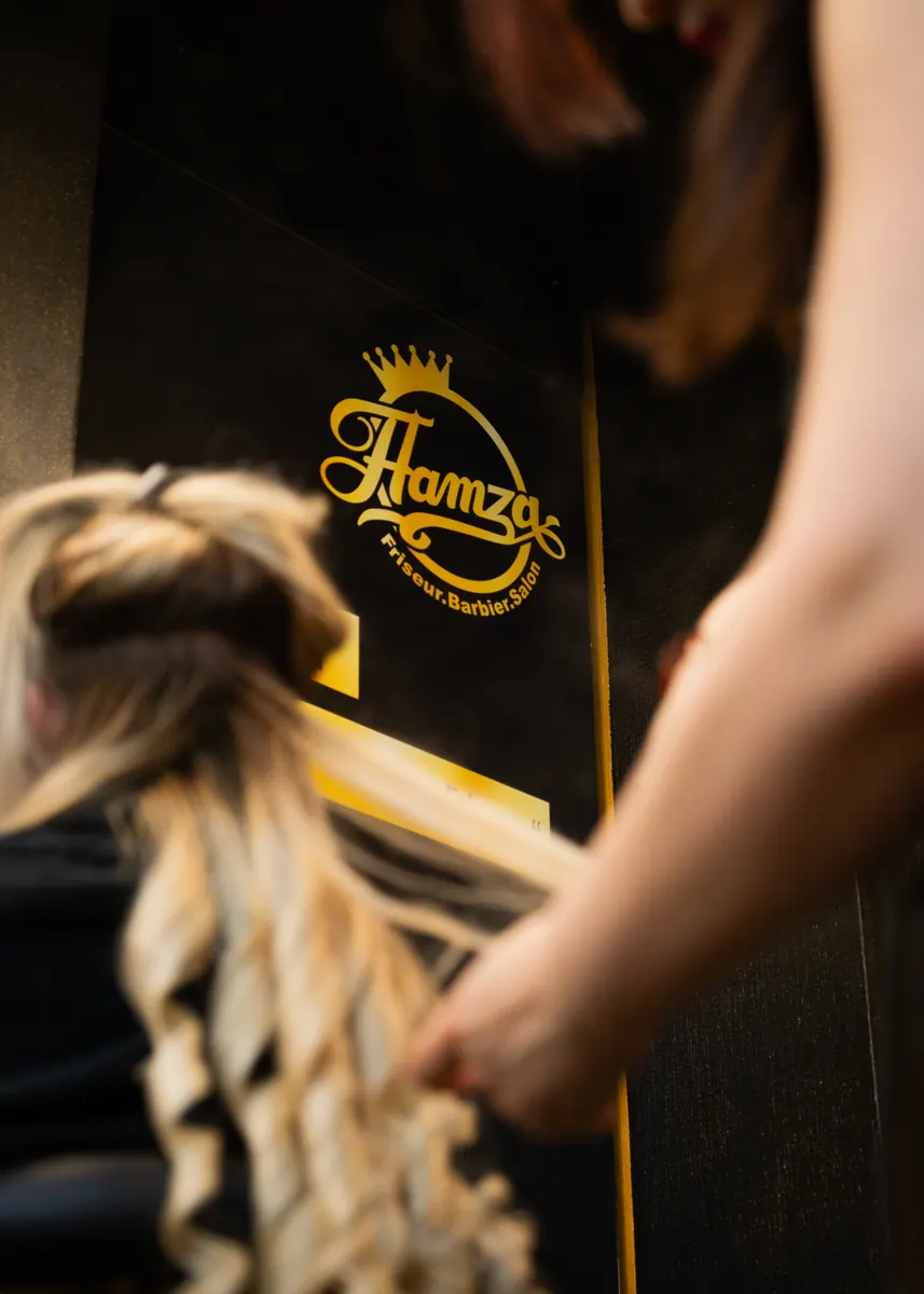 Gestylte Locken vor dem goldenen Hamza-Logo
